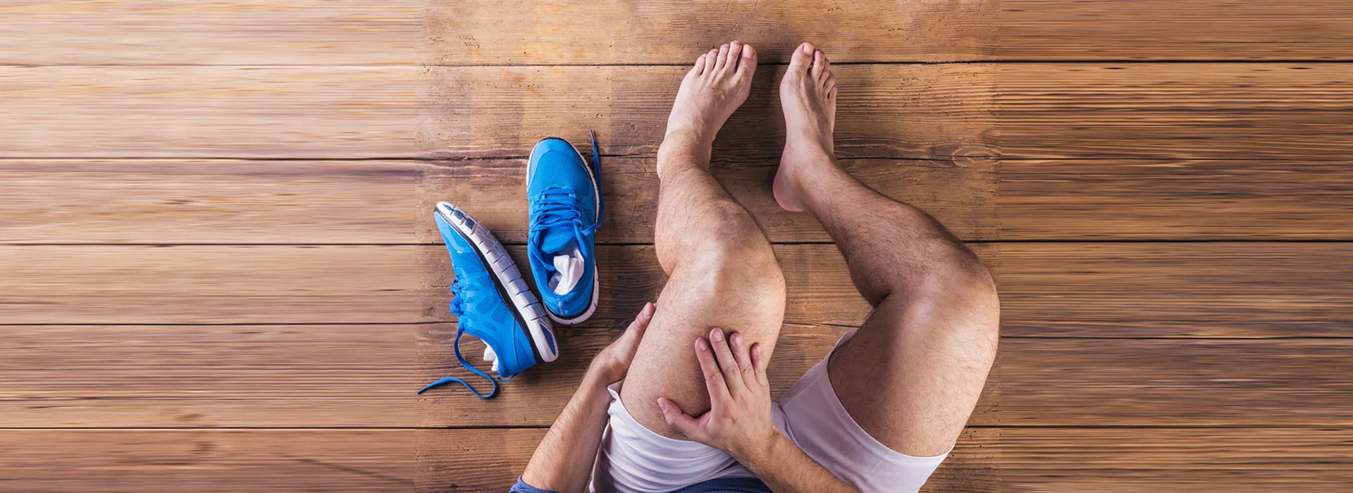 Runner sitting on a wooden floor holding an injured ankle